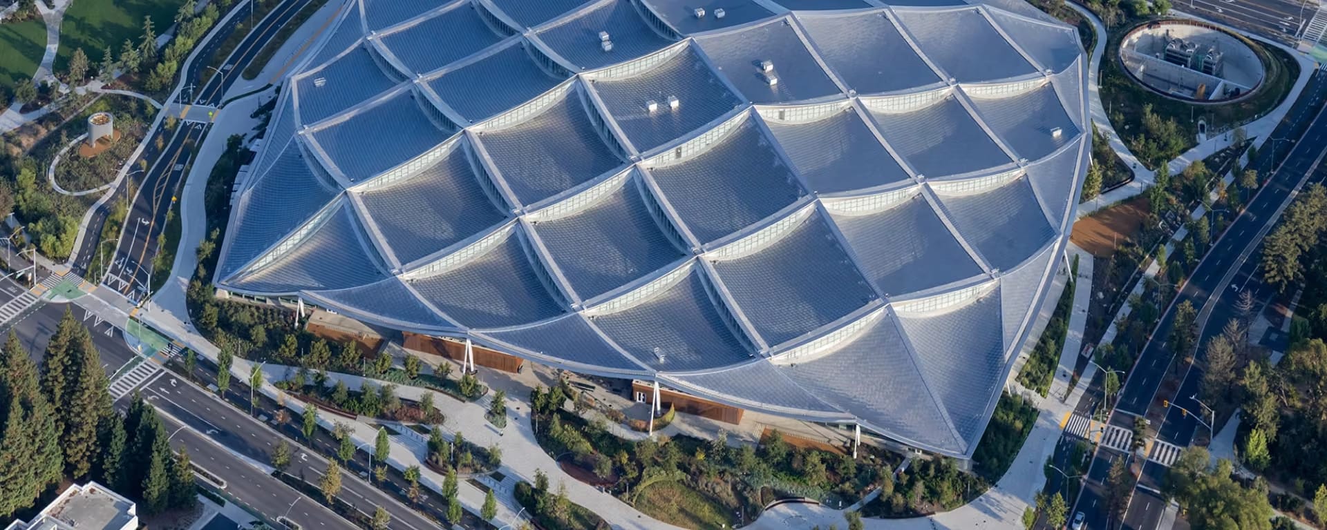 Aerial view of the Google Gradient Canopy building in Mountain View, characterized by its distinctive, large-scale dragon-scale roof structure, surrounded by roads, trees, and walkways.