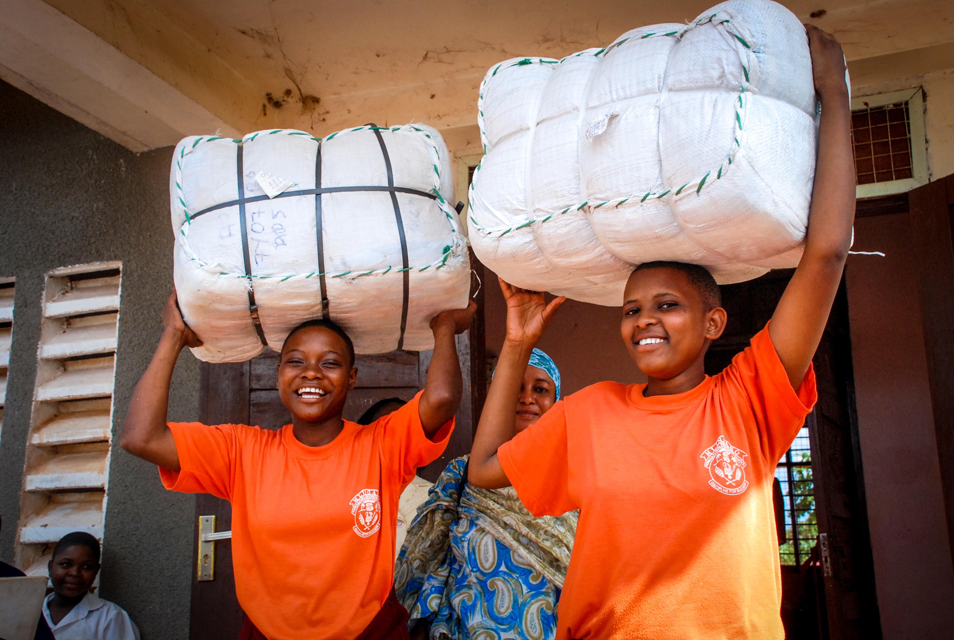 Women in Uganda holding bales of insecticide-treated bednets provided by the Against Malaria Foundation, one of Giving What We Can