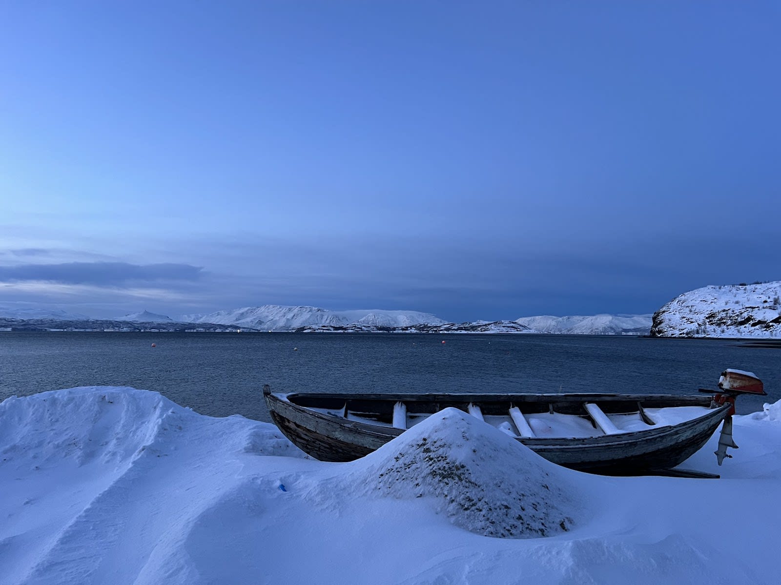 Photo of a snowy fjord with a boat on the shore. From Alta, Norway.