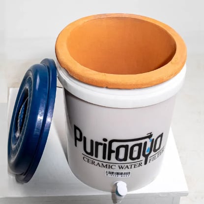 Image of a "Purifaaya" ceramic filter with its lid open, showing both the plastic bucket in the outside and the ceramic filtering element inside it