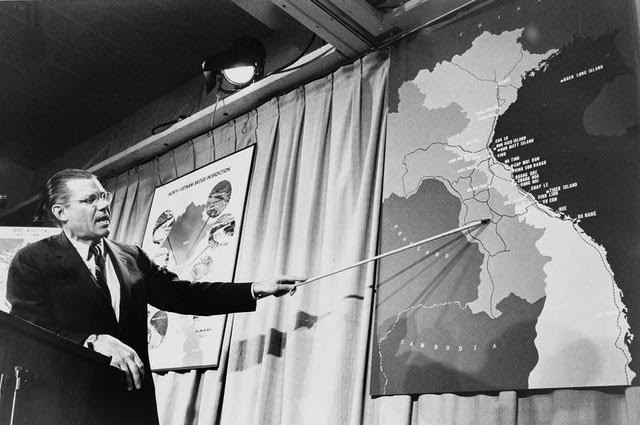 Robert McNamara pointing at a map of Vietnam during a press conference.