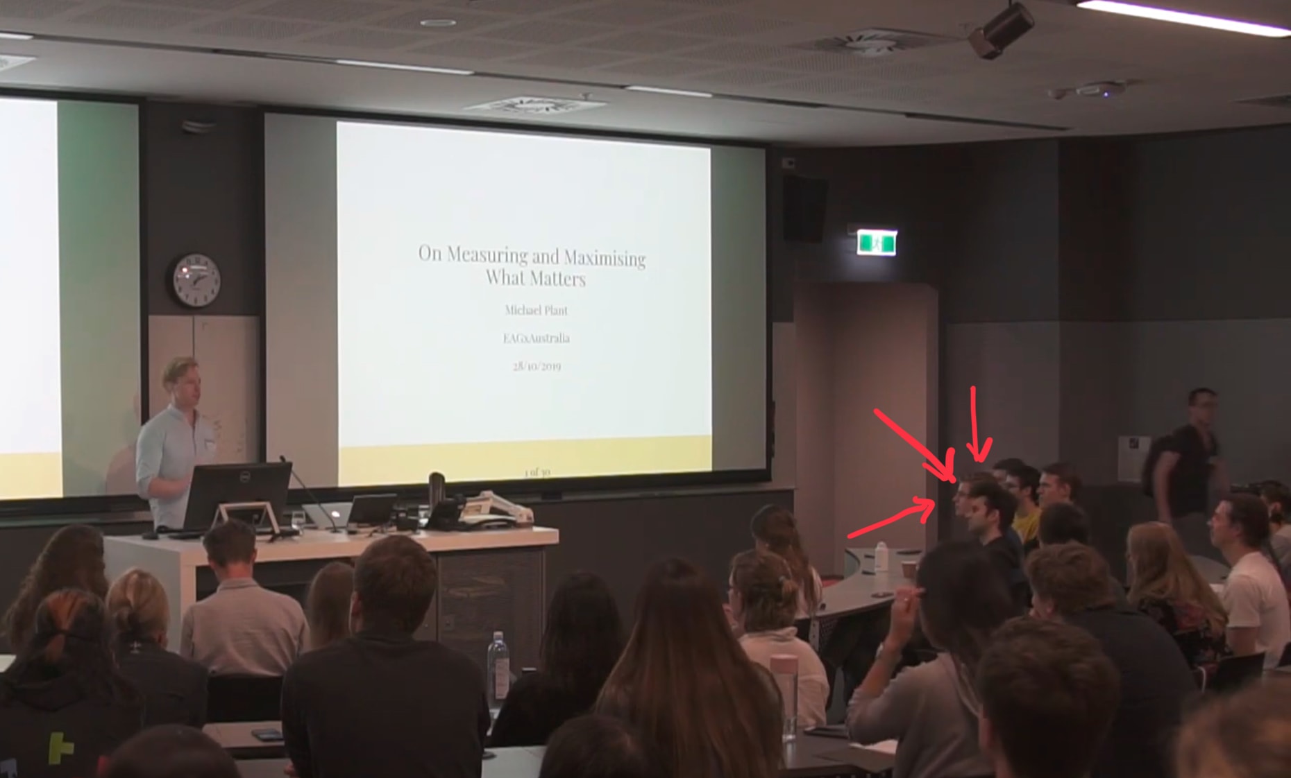 A photo of Michael Plant giving a talk at EAGxAustralia 2019, where I am clearly visible in the audience (demarcated by drawn-on red arrows pointing at me).