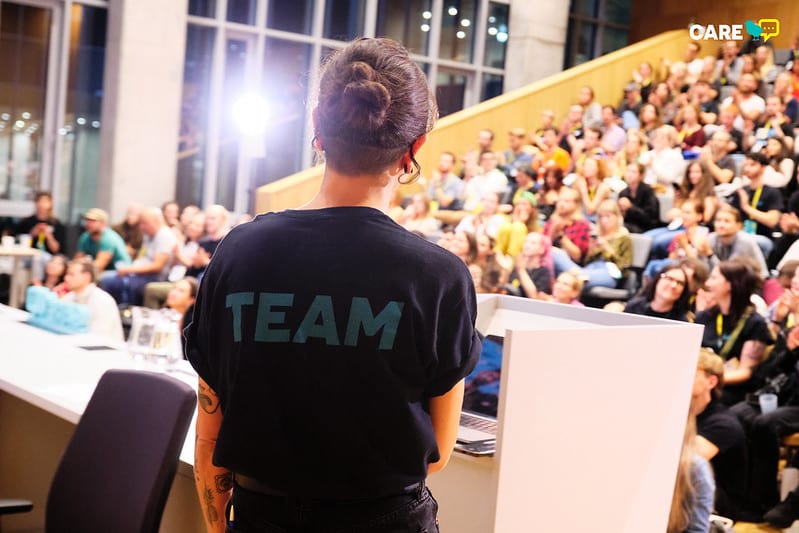 The conference hall with person in a t-shirt with caption "team" standing backwards to the camera.